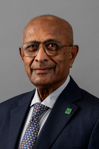 portrait of man wearing a navy blue blazer, multi colored geometric tie, and a light gray collared shirt